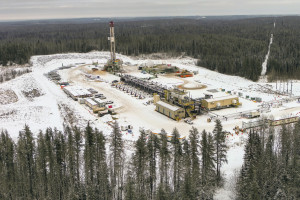 Drilling rig and industrial buildings on snowy clearing surrounded by trees