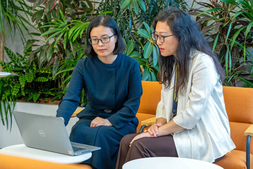 Two employees looking at the computer with greenery behind them