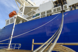 Side of a blue tankership with electrical cords stretching to shore