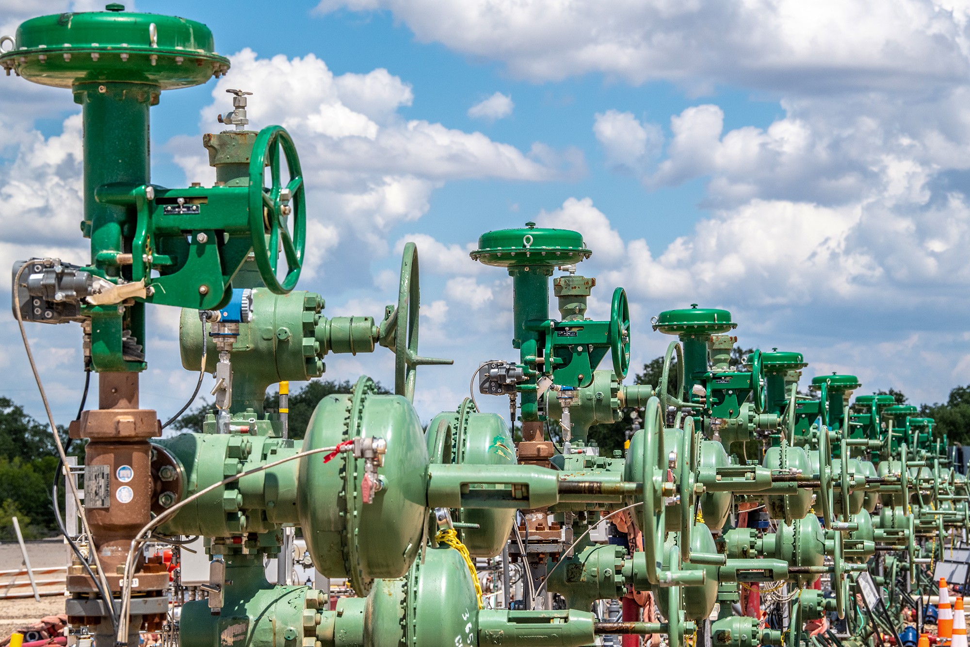 A line of wellheads with a background of blue sky and fluffy clouds