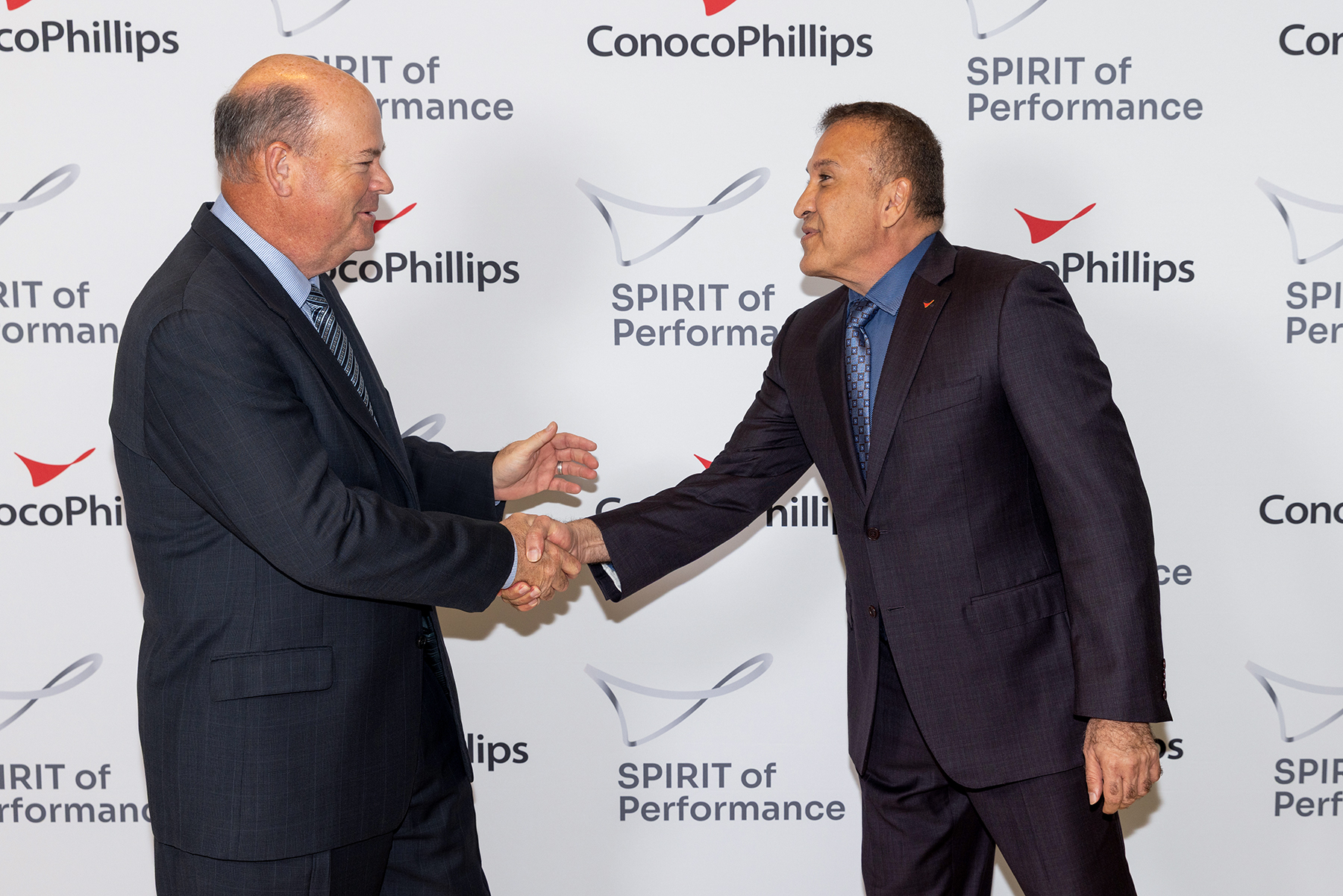 Ryan Lance shakes Dr. Adham's hand in front of SPIRIT Awards photo backdrop