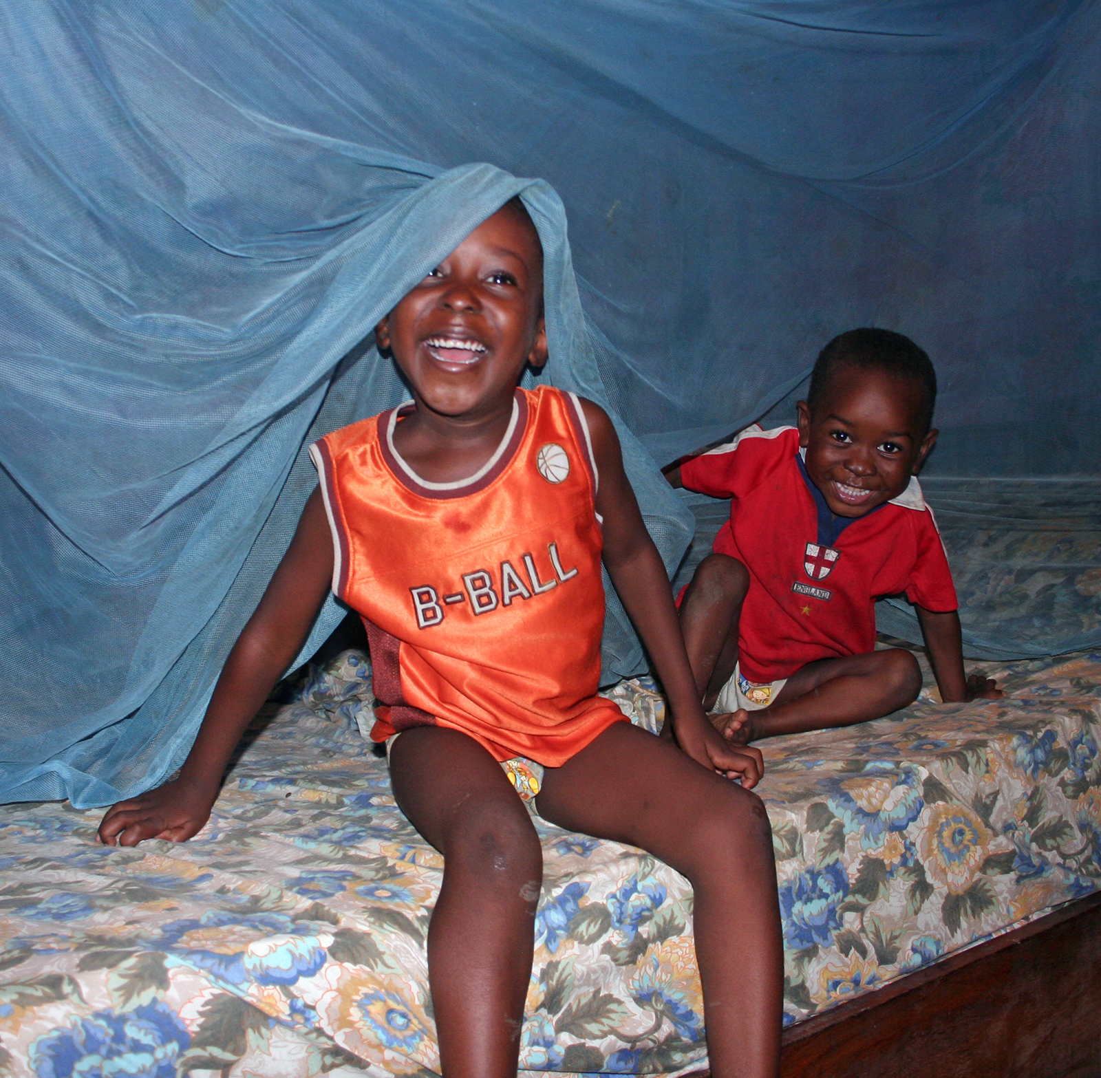Two smiling children on bed with netting above