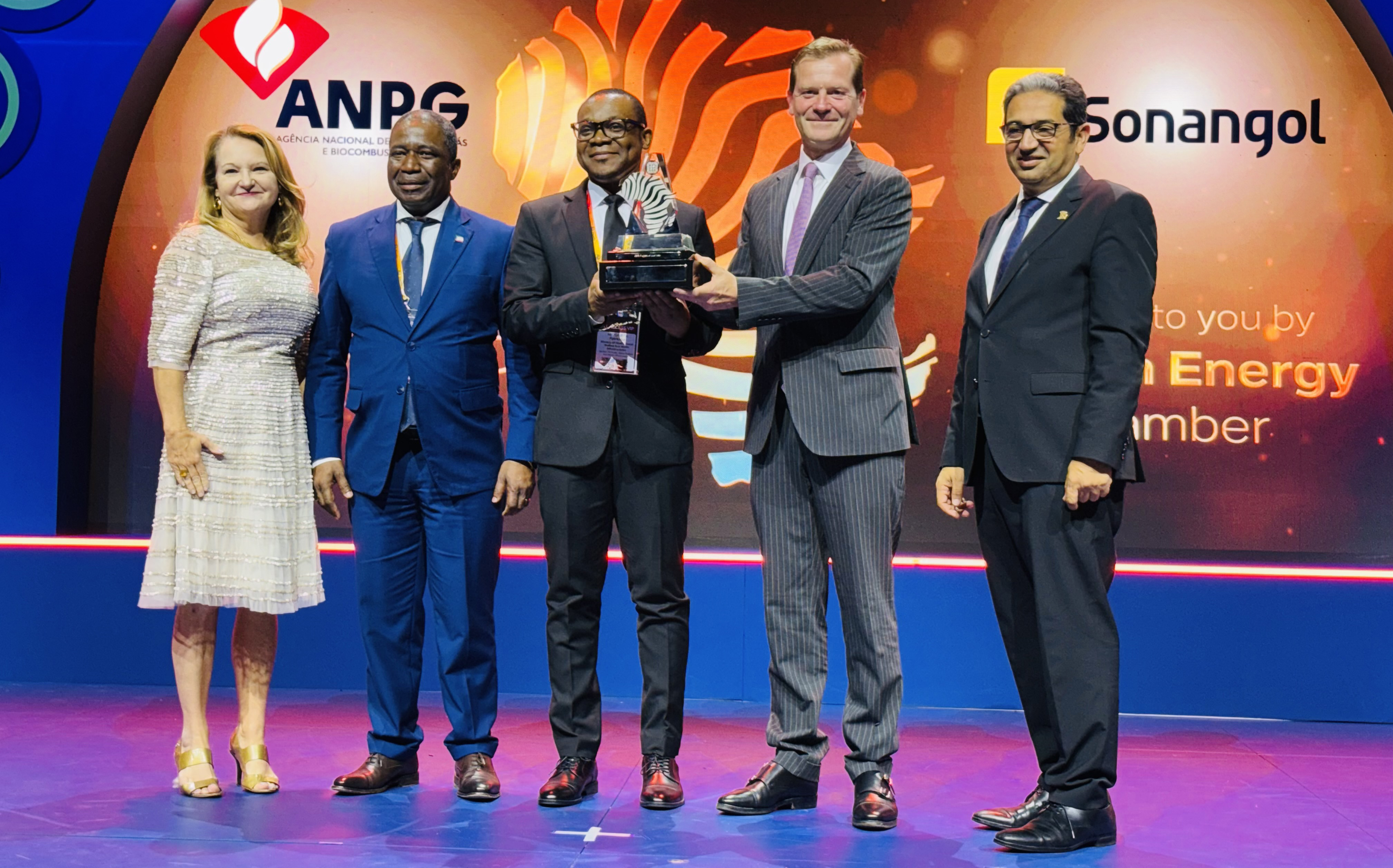 Five people standing on stage in front of colorful backdrop with one person holding award