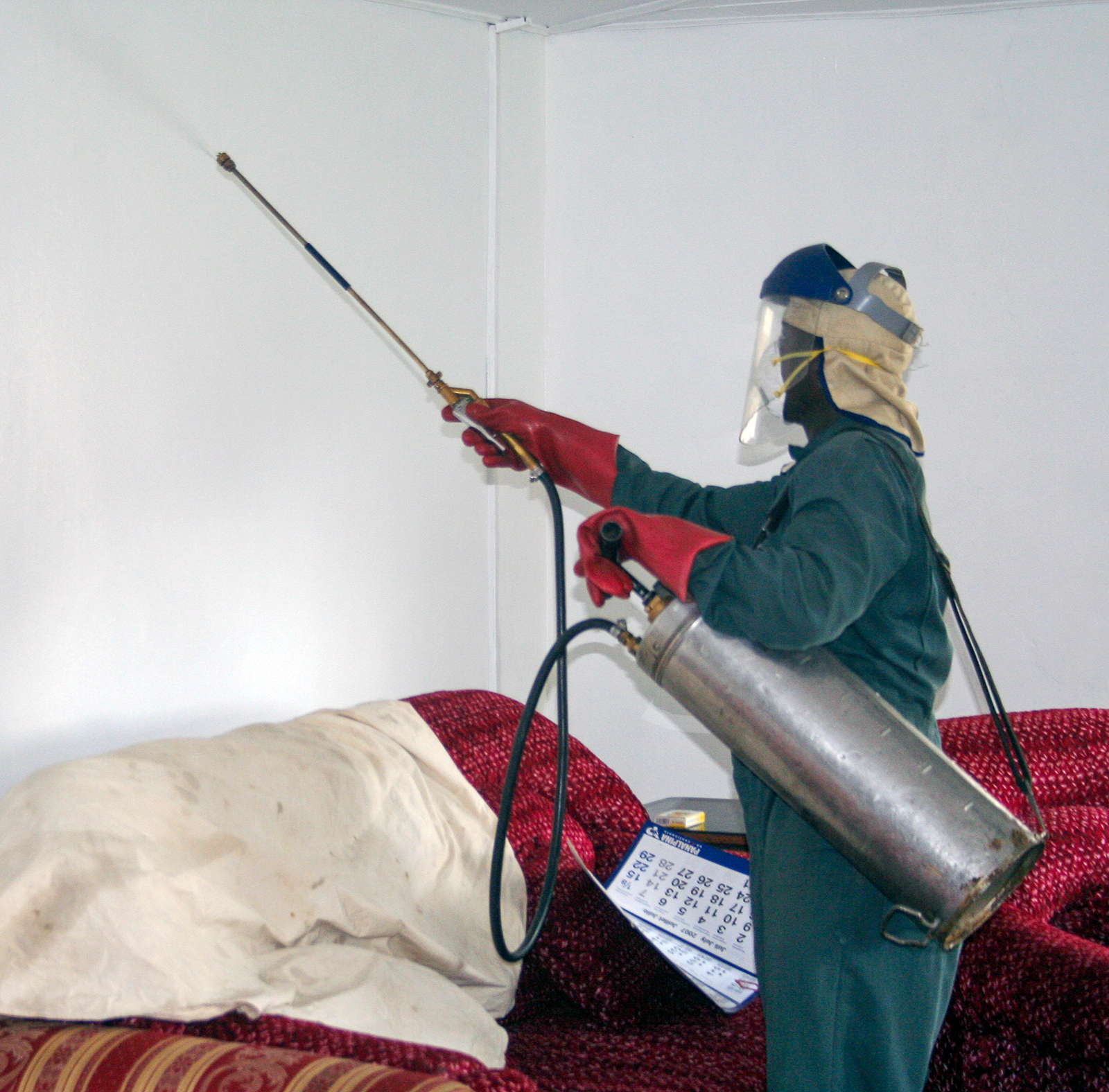 Person in protective gear, holding tank and spraying wall inside a home