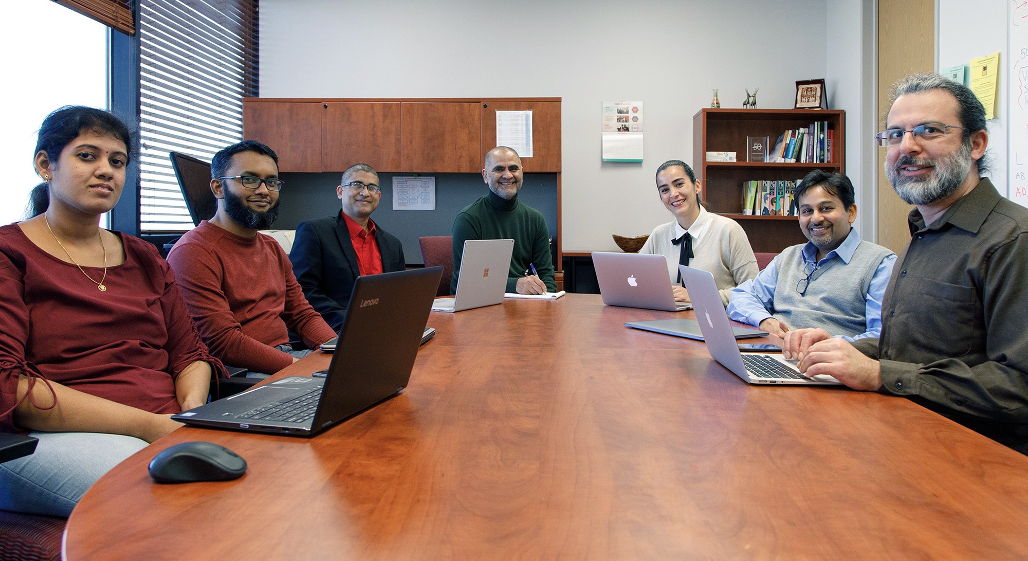 Group of seven people with laptops sitting around conference table