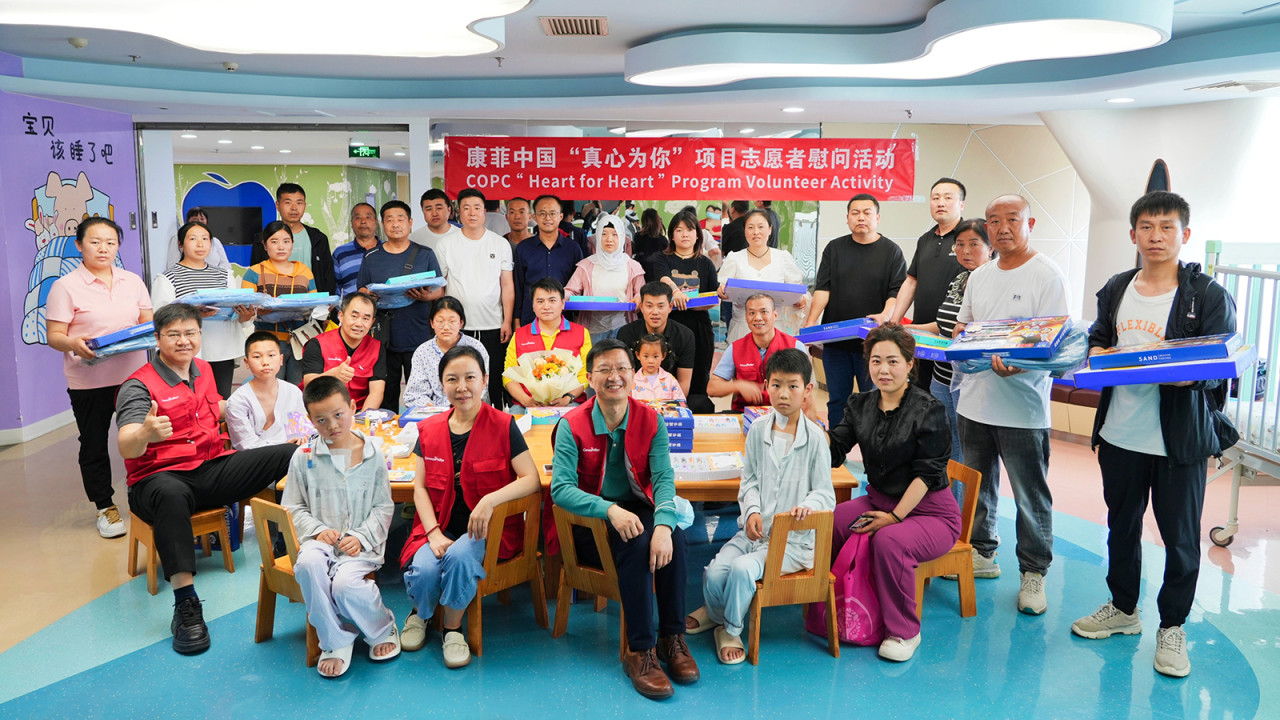Group of roughly 30 people, adults and some children, in children's hospital setting. Many seated at child-size table and chairs.