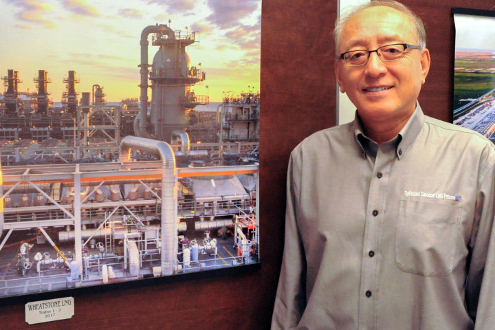 Qi Ma standing near a photo of an LNG facility.