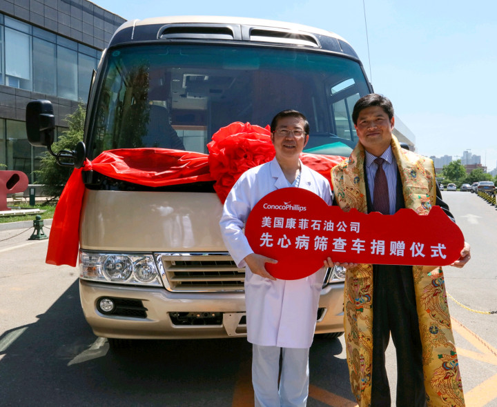 Two men facing camera standing outside in front of a van with red ribbon on the front holding a red key-shaped sign with Chinese lettering and ConocoPhillips logo.