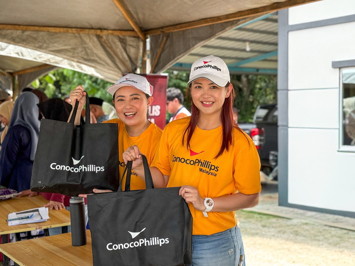 Two smiling volunteers with ConocoPhillips shirts and swag under a tent