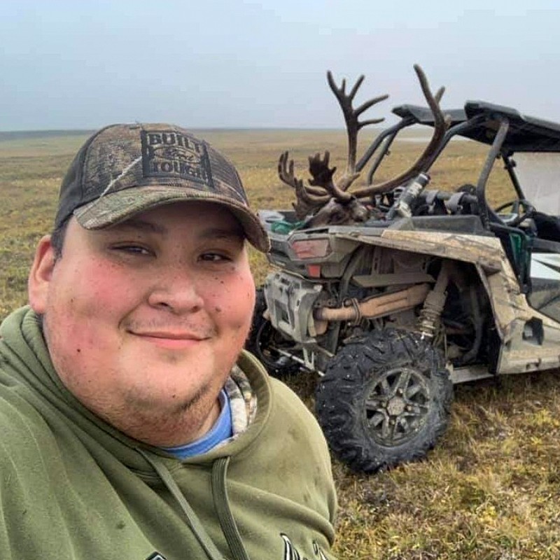 Curtis Ahvakana looking toward camera with deer and vehicle in background