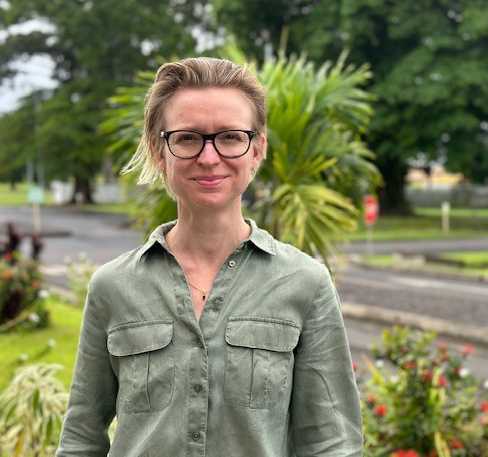 Person standing outdoors with greenery and street in the background
