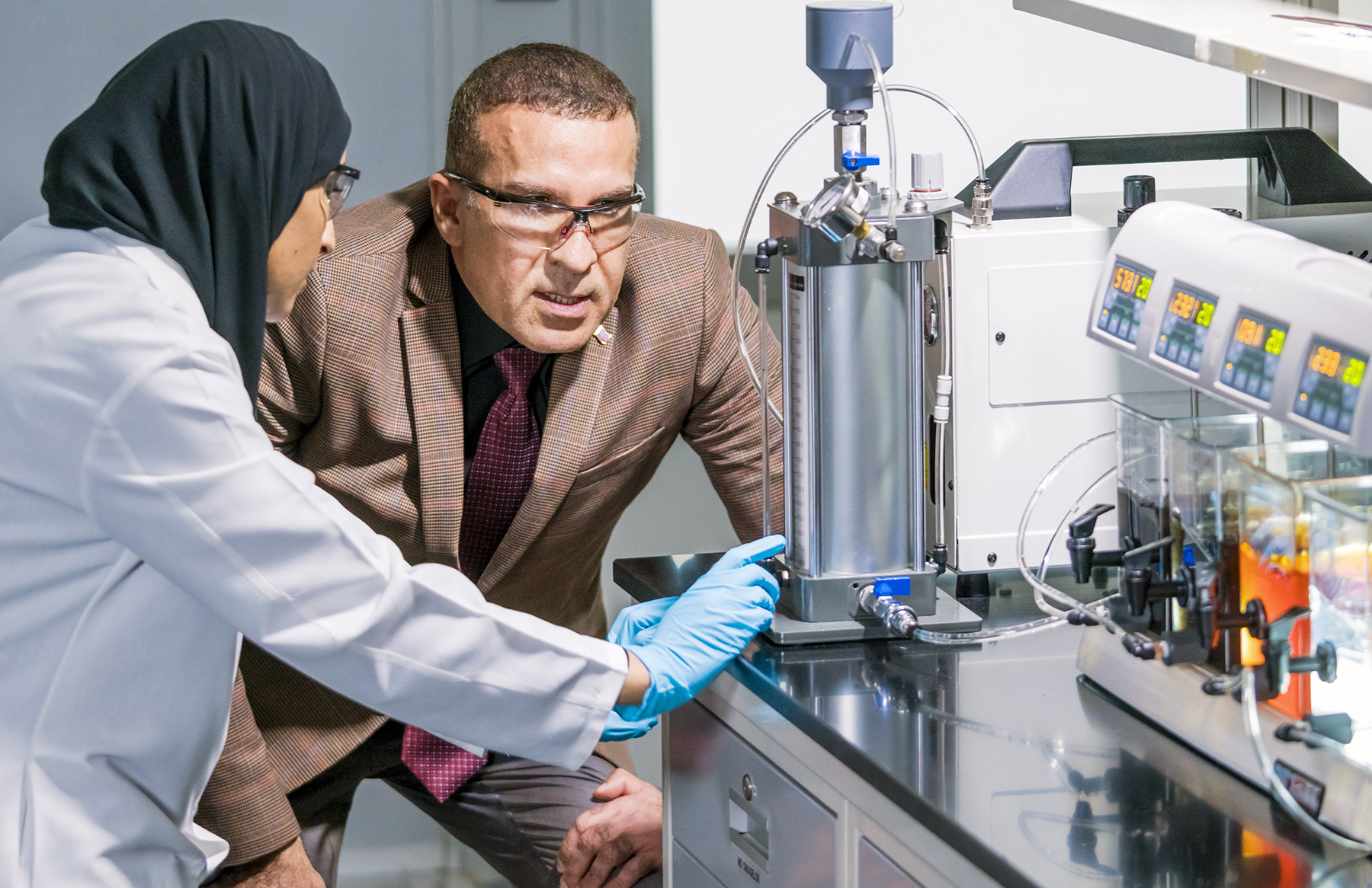 Adham and Al-Mass observe testing equipment in lab