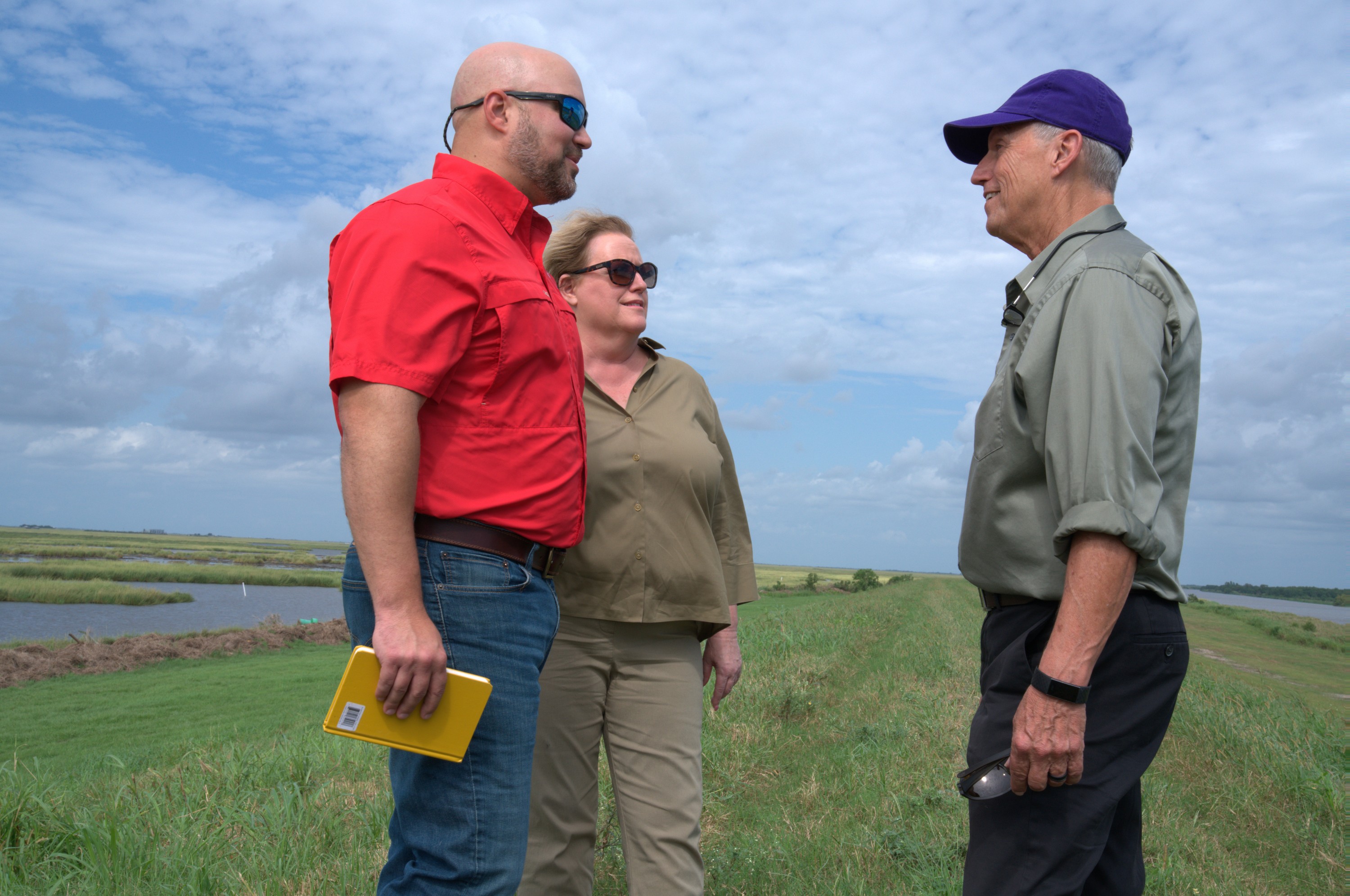 Three people talking outside, marshland in background