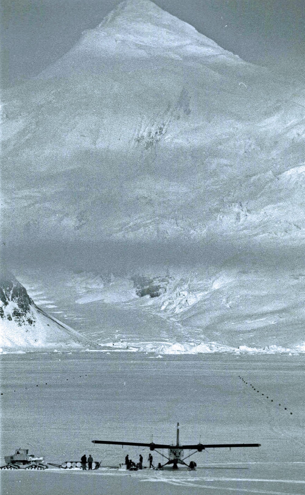 People gathered near plane on ice runway with snow covered mountains in background